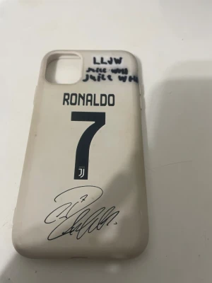 Ronaldo 7 Juventus iPhone Case - Unik iPhone-skal med Ronaldo 7 Juventus-design och autograftryck. Skalets framsida har handskriven text och viss missfärgning, samt tecken på slitage. Passar iPhone med dubbla kameror. Perfekt för fotbollsfans som vill skydda sin mobil med stil iPhone 11