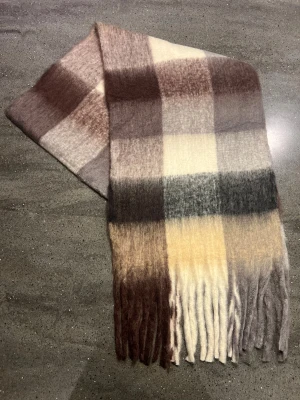 Halsduk - Snygg och fluffig halsduk ( som liknar acne studios) med rutigt mönster i brunt, beige, grått och svart. Lång modell med fransar i ändarna, perfekt att svepa runt halsen för extra värme. Materialet känns mjukt och cozy, passar dig som gillar neutrala färger och klassisk stil.
