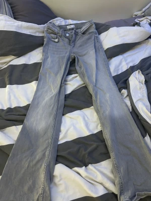 Grå bootcut jeans från Gina Tricot - Snygga ljusgrå jeans från Gina Tricot, modell Perfect Jeans. Byxorna har bootcut-ben och klassisk femficksdesign. Tillverkade i mjukt jeanstyg med en skön passform och normal midja. Perfekta för dig som gillar en stilren och enkel look.