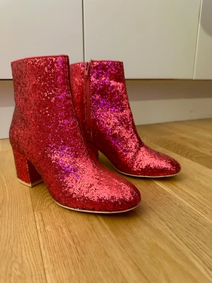 Glittriga rosa boots med klack, strl 37 /läs beskrivning. - OBS läs innan!  Har aldrig haft skorna på mig bara inomhus på julafton . Skorna hängde på Nelly event - fashion show jag fick dem efter showen. Det finns små hål under. Annars är skorna i nytt skick. Passar perfekt till en fest eller liknande.  Verkligen sjukt snygga boots i glittrigt röd/rosa med blockklack och rund tå. Skorna har dragkedja på sidan och är täckta av glittriga paljetter som verkligen sticker ut. Perfekta för dig som vill ha statement-skor med extra bling.