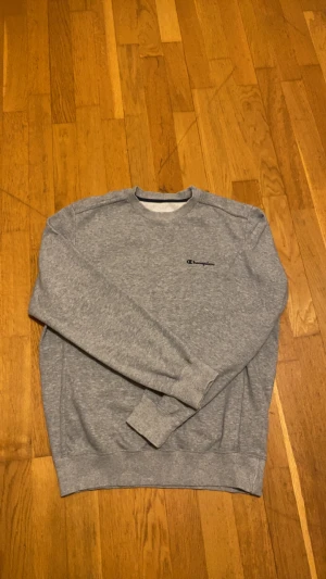 Grå sweatshirt från Champion - Säljer en grå sweatshirt från Champion i storlek M. Tröjan har klassisk rund hals, ribbade muddar och Champion-logga broderad på bröstet. Mjuk insida och enkel stil som funkar till jeans eller joggers. Perfekt för chill dagar. Den är extremt skön att ha på sig och samtidigt riktigt clean.