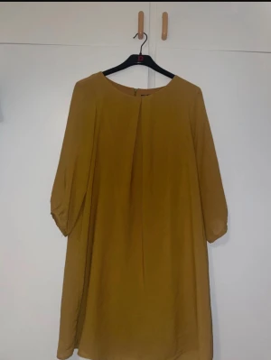 Beige klänning från H&M med trekvartsärm - Säljer en stilren beige klänning från H&M i storlek 44. Klänningen har en rak passform, trekvartsärmar och rund halsringning. Materialet är mjukt och lätt polyester, med en diskret dragkedja i ryggen för enkel påklädning.