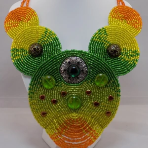 Färgstarkt statement halsband i pärlbroderi - Unikt halsband med stora cirkulära pärlplattor i grönt, gult och orange. Dekorerat med gröna glaspärlor, metallknappar och små hjärtformade detaljer. Handgjort och riktigt iögonfallande, perfekt för dig som gillar färg och statement-smycken.