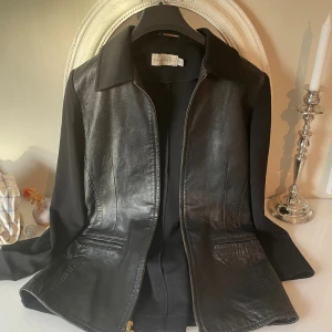 Svart skinnjacka Florine Wachter - Svart jacka från Florine Wachter med skinn framtill och släta tygärmar och rygg .det är bara framme som är i skinn .jackan på inesidar vid fickor på båda sidor är liten slitage,som ni kan se på sista bild .Jackan har klassisk krage, dragkedja och två fickor framtill. Snygg, rak passform som funkar till många stilar. Perfekt för dig som gillar en stilren och edgy look.