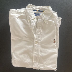 Vit skjorta Polo Ralph Lauren S - Vit skjorta från Polo Ralph Lauren i slim fit broderad logga på bröstet. Tillverkad i bomull och har knappar framtill. Perfekt för en clean och stilren look. Säljer pga att den är för liten för mig den har knappt andvänts bara några enstaka gånger