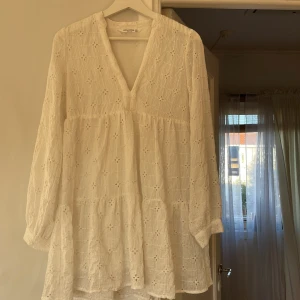Vit klänning - Jag säljer nu en vit klänning i broderat tyg. Den har lång ärm med knappar längst ner, underkjol och är luftig. Uppklädd till fest men även skön till stranden. Använd 1 gång. Skick 10/10