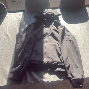Svart vindjacka Jack & Jones Core M - Svart vindjacka från Jack & Jones Core med huva och dragkedja framtill. Jackan har två stora fickor och ribbade muddar vid ärmsluten. Perfekt för dig som gillar en clean och enkel stil.