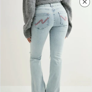 Nelly ljusblå bootcut jeans - Säljer ett par ljusblå jeans från Nelly med bootcut passform. Jeansen har klassiska fem fickor, snygga slitningar vid knäna och broderade detaljer på bakfickorna. Materialet är mjukt denim och midjan är låg. Perfekta för dig som gillar coola detaljer.