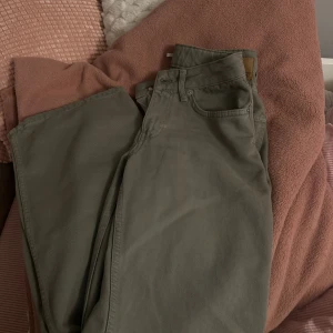 Gröna raka jeans från 157 - Snygga gröna jeans från 157 med klassisk femficksdesign och raka ben. Byxorna har bälteshällor, knapp och dragkedja fram samt en neutral grön färg som passar till det mesta. Materialet är slitstark bomull och modellen har en straight fit. Xxs-xs