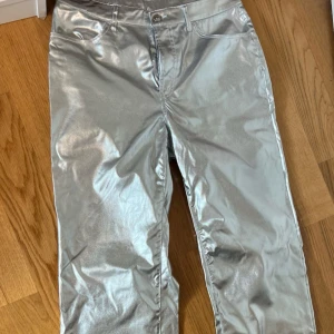 Silvriga raka byxor i metallic - Säljer ett par riktigt snygga byxor i metallic silver med rak passform. Byxorna har klassisk femficksdesign och stängs med knapp och dragkedja. Perfekta för dig som vill sticka ut med en futuristisk vibe. Endast använd en gång! 