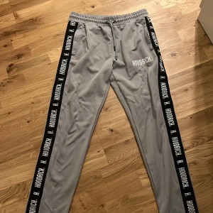 Grå Hoodrich Byxor - Snygga grå mjukisbyxor från Hoodrich med svarta logoband längs sidorna och vit HOODRICH-tryck på benet.