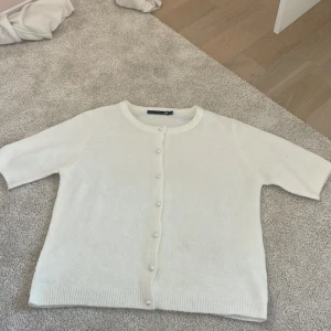 Vit kofta med pärlknappar från 157 - Superfin vit kofta från lager 157 med pärlknappar framtill. Koftan har rund halsringning, och är stickad i ett mjukt material. Perfekt att slänga över en topp för en clean och söt look. Den är helt ny pris kan diskuteras 