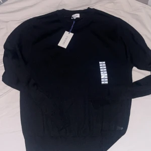 HELT NY Svart stickad tröja i merinoull från SANDÖ - Stilren pullover i merinoull som passar till både chinos och jeans. Säljer då jag skulle velat ha blå istället och öppet köp hade gått ut • Pullover i 100% merinoull • Ribbstickade kanter • Rund halsringning.