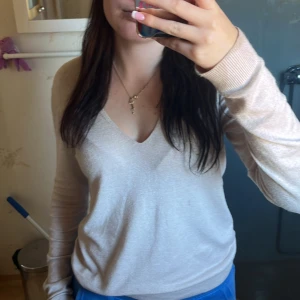 Beige v-ringad stickad tröja - Säljer en ljusbeige stickad tröja med v-ringning och långa ärmar. Tröjan har en klassisk och enkel design som är lätt att matcha med olika outfits. Perfekt för dig som gillar en stilren och mjuk look.