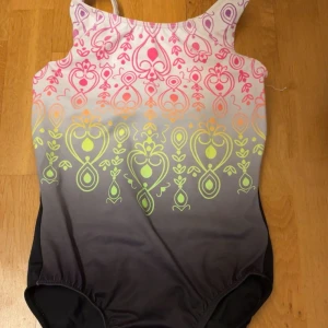 Färgglad gymnastikdräkt med mönster - Snygg gymnastikdräkt med coolt grafiskt mönster i rosa, gult och orange på en bas som tonar från vitt till svart. Perfekt för träning och tävling. Bekväm passform och breda axelband. Färgerna poppar verkligen och ger en unik look.