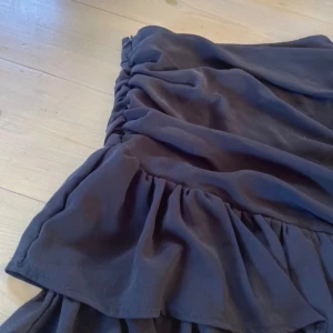 Svart volangkjol från Boohoo - Supersnygg svart kjol från Boohoo med volanger och draperad design. Storlek S med dragkedja i midjan vilket gör det smidigt att sätta på/ ta av. Nytt skick☺️☺️