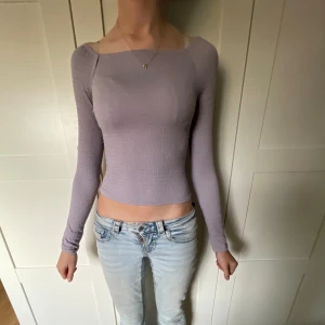 Ljuslila långärmad topp från Kappahl - Säljer en ljuslila långärmad topp från Kappahl i storlek 146/152. Toppen är croppad med smockad, ribbad struktur och har en snygg, tight passform. Perfekt att styla med jeans eller kjol för en chill look.