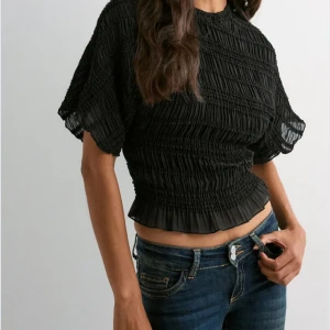 Jättefin svart smockad blus med volangkant från Nelly - Jättefin tröja från Nelly! Tröjan är helt ny, aldrig använd, ordinariepris 299kr! Går att ha både till fest och till en vanlig skoldag då den går att klä upp och klä ner. Supersnygg svart blus med smockad struktur och volangkant nertill. Blusen har korta, luftiga ärmar för en trendig look. Tillverkad i ett lätt, transparent material som ger en cool och luftig känsla.