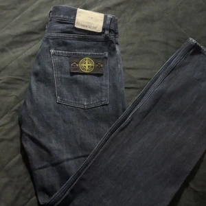 Stone Island jeans blå W30 L34 - Snygga blå jeans från Stone Island med klassisk femficksdesign och ikonisk patch på bakfickan. Jeansen har raka ben och normal passform, tillverkade i slitstarkt denim med subtil tvättad look. Perfekt för dig som gillar streetwear och vill sticka ut.