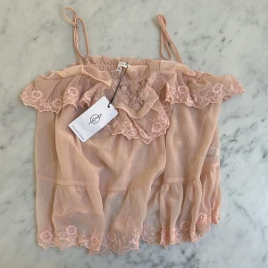 Rosa spetslinne från Stradivarius - Supersött ljusrosa linne från Stradivarius med tunna axelband, volangkant och broderade spetsdetaljer. Luftigt tyg i polyester med romantiska blommönster och transparent känsla. Perfekt för en feminin och trendig look.