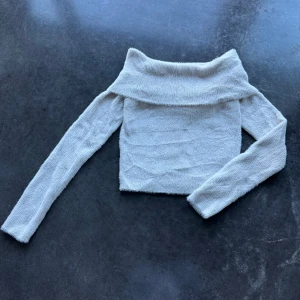 Beige offshoulder topp Bershka - Supermjuk och fluffig beige offshoulder topp från Bershka. Croppad modell med långa ärmar och bred krage som vilar snyggt över axlarna. Perfekt för dig som gillar en cozy men trendig vibe.