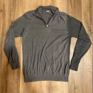 Mörkgrå halvzip tröja Dressmann - Mörkgrå långärmad tröja från Dressmann med ribbad krage och half zip-dragkedja. Tillverkad i mjuk bomull, perfekt för lager-på-lager. Enkel och stilren design som funkar till många outfits. Skick 9/10