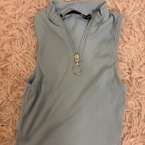 Ljusblå ribbad ärmlös topp från lager 157 - Säljer en ljusblå ribbad ärmlös topp från lager 157 med hög krage och cool dragkedja framtill med ringdetalj. Toppen har en slim passform och är perfekt för att skapa en trendig look. Supersnygg att styla med jeans eller kjol!