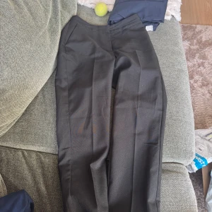 Svarta kostymbyxor från ASOS Design - Snygga svarta kostymbyxor från ASOS Design i klassisk rak modell. Byxorna har pressveck framtill, sidfickor och en stilren look som passar perfekt till en dressad outfit. Materialet känns mjukt och följsamt, och midjan är normalhög.