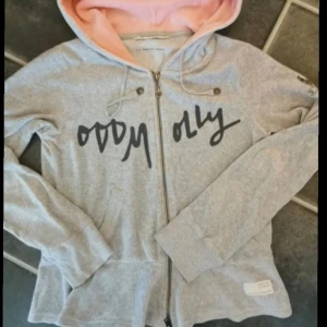 Underbar grå hoodie från Odd Molly med rosa huva, storlek Small - Grå hoodie från Odd Molly med dragkedja, svart tryck framtill och rosa insida på huvan. Tröjan har snörning vid huvan, långa ärmar och en snygg patch på ena ärmen. Perfekt för chill dagar och snygg streetstyle. Storlek 1, Small.  Mycket fint skick, djur och rökfritt hem. Måste ses!:)