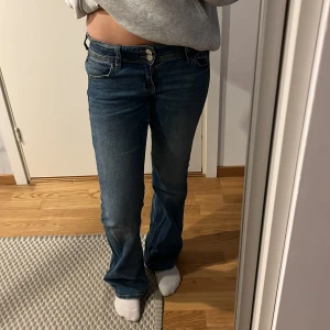 Blå bootcut jeans med fickdetalj - Snygga blå jeans med bootcut passform och låg midja. Jeansen har fickor med knapp bak. Perfekta för dig som gillar en avslappnad men ändå trendig stil. Få tecken på användning.