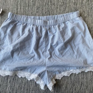 Blåvita randiga pyjamasshorts med spets - Snygga blåvita pyjamasshorts från Calypso St. Barth i 100% bomull. De har tunna ränder och elastisk midja för skön passform. Nederkanten är dekorerad med vit spets som ger en extra touch.  Mått Midjan: ca 43 cm Total längd: ca 37 cm  100% bomull  Kommer från ett djur och rökfritt hem.