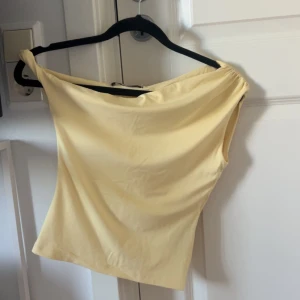Gul offshoulder topp från Gina Tricot - Säljer en ljusgul offshoulder topp från Gina Tricot i storlek XS. Toppen har en stilren och enkel design med mjukt, stretchigt material som sitter snyggt mot kroppen. Perfekt för dig som gillar minimalistisk stil och vill ha något som sticker ut med sin färg.