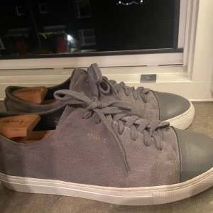 Axel arigato clean 90 suede cap - Snygga grå sneakers från Axel Arigato med mocka på sidorna och tå i grått skinn. Klassisk rund tå, vita platta sulor och snörning framtill. Perfekt för dig som gillar stilrena och minimalistiska skor med premiumkänsla. Passar 43 också
