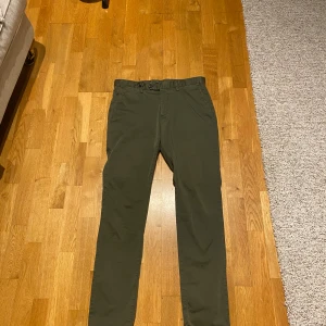 Mörkgröna chinos med slim passform - Snygga mörkgröna chinos med slim passform och klassisk design. Byxorna har framfickor, bakfickor med knapp och bälteshällor. Perfekta för dig som gillar stilrena och enkla byxor med smal siluett.