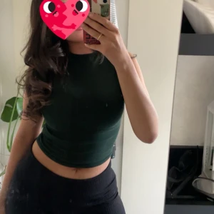 Mörkgrön croppad topp från Zara - Säljer en mörkgrön croppad ärmlös topp från Zara. Toppen har en tight passform och är tillverkad i ribbad bomullsmix. Perfekt till jeans eller kjol för en clean och stilren look.