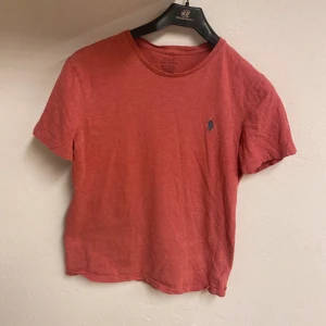 Röd t-shirt från Polo Ralph Lauren - Snygg röd t-shirt från Polo Ralph Lauren med klassisk blå broderad logga på bröstet. Modellen är slim fit och har rund hals samt korta ärmar. Tillverkad i mjuk bomull som känns skön mot huden. Perfekt för dig som gillar stilrena och tidlösa plagg.