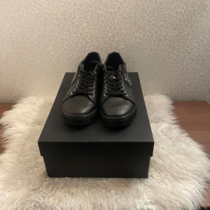 Svarta sneakers från Philipp Plein - Snygga svarta sneakers från Philipp Plein med metallfärgad logga på sidan och plös. Skorna har snörning, rund tå och platt sula med mönstrad undersida. Tillverkade i skinn med coola detaljer i silver, bara använda 1 gång. Perfekta för dig som gillar exklusiv stil. 