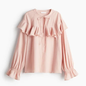 Ljusrosa blus med volang  - Supersöt ljusrosa blus med bred volang över bröstet och långa puffiga ärmar med smock och volang vid ärmslut. Lite mer rosa än på bild