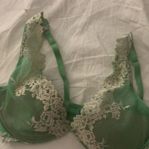 Grön spets-bh med blommigt mönster - Snygg grön bh med dekorativ spets och blommigt broderi i beige. Bh:n har justerbara axelband och transparent mesh som ger en cool look. Perfekt för dig som gillar detaljer och vill ha något extra under kläderna.