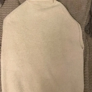 Beige stickad väst från NA-KD - Säljer en beige stickad väst från NA-KD i storlek S. Västen har en ribbad struktur och hög hals, vilket ger en clean och modern look. Perfekt att styla över en skjorta eller t-shirt för en chill vibe.