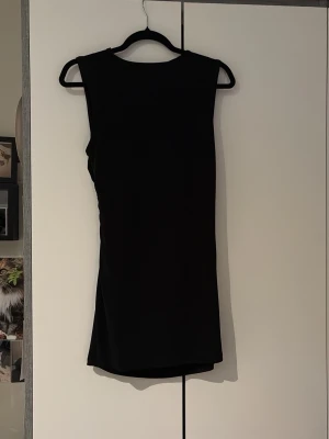 Svart ärmlös kortklänning 157 - Säljer en svart, enkel och stilren kortklänning från 157 i storlek XS. Klänningen är ärmlös med rak passform och rund halsringning. Perfekt basplagg att styla med accessoarer eller jacka.