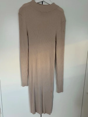 Beige ribbad långklänning  - Säljer en beige långklänning i storlek 36. Klänningen är ribbstickad med lång ärm och har en högre krage. 