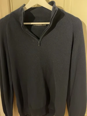 Mörkblå stickad tröja med half zip - Snygg mörkblå stickad tröja från Stenströms med half zip i halsen. Tröjan har långärmade raglanärmar och en ribbad krage som ger en cool och avslappnad look. Perfekt för dig som gillar klassisk stil med en modern twist.