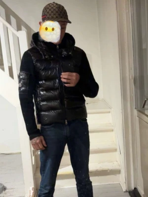 Svart Moncler pufferjacka med huva - Säljer en svart pufferjacka från Moncler med glansig framsida och huva. Jackan har stickade ärmar och detaljerad Moncler-logga (finns nfcs tagg) på ena ärmen. Dragkedja framtill och praktiska fickor. Perfekt för dig som vill rocka sånt fett