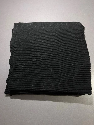 Svart glittrig halsduk  - Svart stickad halsduk med ribbad struktur och diskret glittrande tråd. Halsduken är tillverkad i ett mjukt stickat material som känns skönt mot huden. Varm och skön och perfekt att ha över axlarna till en festklänning 🥳Storlek 140x80. Mycket bra skick, enstaka tråddragning som inte stör helheten (se bild). Säljs på flera sidor, först till kvarn. 