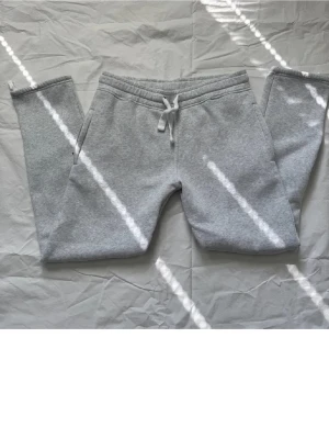 RUSSE MERCH Byxor - Säljer ett par grå mjukisbyxor från Russe merch  storlek M. Byxorna har snörning i midjan, sidofickor och en bakficka. Tillverkade i mjukt bomullsmaterial som är skönt mot huden. Perfekt för chill dagar och avslappnade stunder. Dom har ett litet hål på framsidan som knappt syns fråga om fler bilder ifall ni vill se hålet annars ser dom helt nya ut