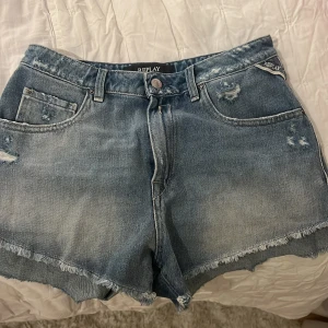 Blå jeansshorts från Replay - Snygga blå jeansshorts från Replay med slitna detaljer och fransig kant. Perfekta för en avslappnad stil. De har en klassisk femficksdesign och knappgylf. Midjan 26. Använda ett fåtal gånger, är som nya💕