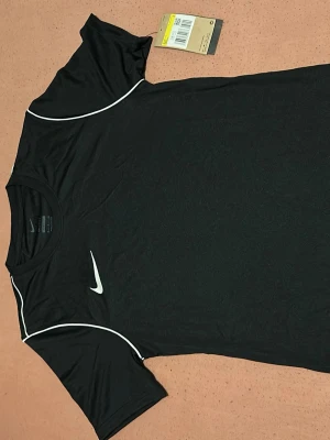 Nike Dri-Fit svart t-shirt herr S - Nike Dri-Fit t-shirt i svart med vit logga och vita detaljer längs axlarna. Slim fit-modell i lätt och funktionell polyester som andas. Perfekt för träning och sport, men inte bara för de man kan använda den för allt. Tshirten är helt ny och helt oanvänd. Klassisk rund hals och korta ärmar. Pris kan diskuteras vid snabb affär🥰