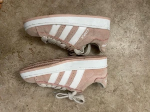 Adidas Campus rosa sneakers - Säljer ett par Adidas Campus sneakers i ljusrosa mocka med vita ränder och vit sula. Skorna har klassisk snörning och platt sula, samt rund tå. Perfekt för dig som gillar retrostil och vill ha något som sticker ut lite extra.