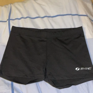 Svarta träningsshorts från SOC - Svarta shorts från SOC, perfekta för träning. De har en enkel design med elastisk midja och är tillverkade i ett syntetmaterial som andas, TCS Air-teknologi. Logga på benet och smidig passform som ger rörelsefrihet.
